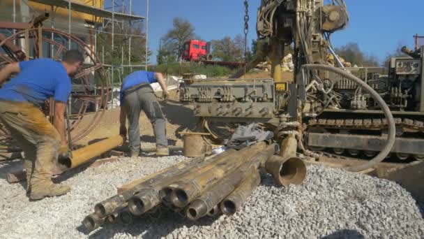 FECHAR UP: Dois construtores masculinos trazer um tubo de metal para perfurar equipamento no local de construção — Vídeo de Stock