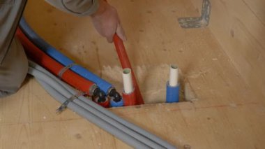 Tanınmayan tesisatçı hortumları ahşap zemindeki bir delikten aşağı itiyor..