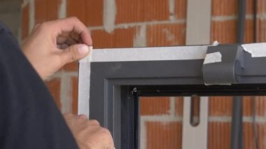 Becerikli adam siyah pencere çerçevesini korumak için beyaz yapışkan bant kullanıyor..