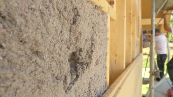 CLOSE UP: група робітників дме ізоляцію целюлози в дерев'яні стіни . — стокове відео