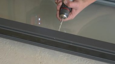 Müteahhit pencere çerçevesinde bir delik açmak için kablosuz matkap kullanıyor..