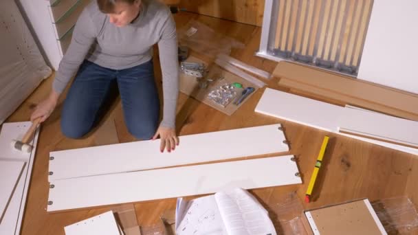 Молодая женщина, переезжающая в свою новую квартиру, собирает белый комод — стоковое видео