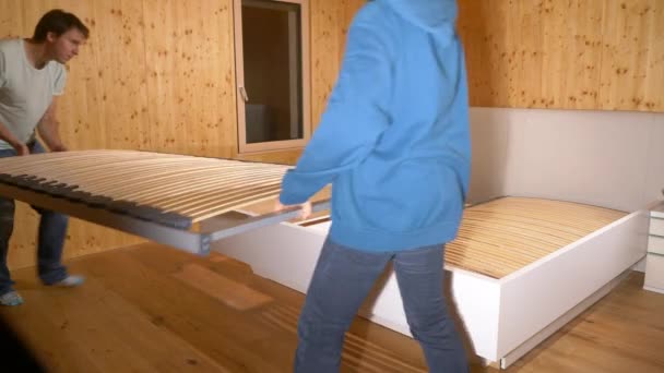 Genç çift yeni evlerinde büyük bir yatak yapmak için birlikte çalışıyor.. — Stok video