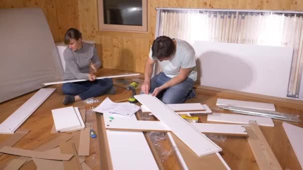 Mladý pár sedí na podlaze a sestavuje postel ve svém novém domově.. — Stock video