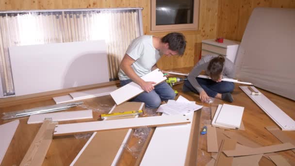 AFSLUITEN: Jonge echtpaar zit op de vloer en monteert meubels in hun nieuwe huis. — Stockvideo