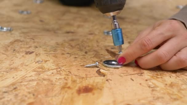 CERRAR: Mujer sujeta una lavadora de metal en una placa de madera contrachapada con un taladro de potencia. — Vídeo de stock