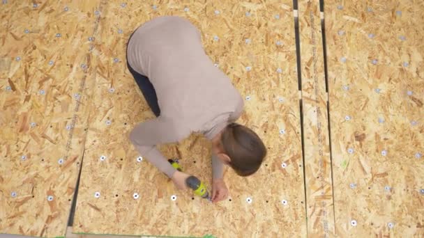 ARRIBA: Mujer sujeta arandelas de metal en una placa de madera contrachapada con un taladro de potencia. — Vídeo de stock