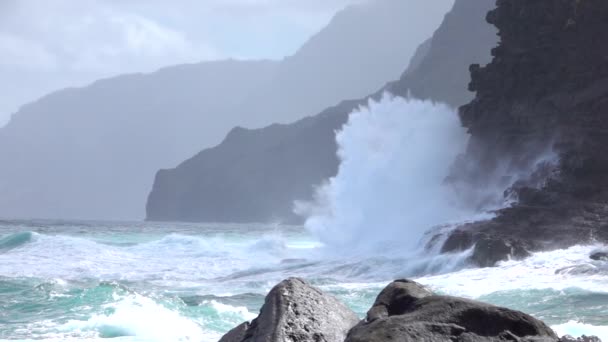 MOTION SLOW : Des vagues de mer déchaînées se brisent et pulvérisent sur le rivage volcanique ensoleillé. — Video