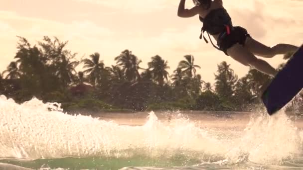 CLOSE UP: Vrouwelijke kitesurfer rijden in Zanzibar springt en doet een superman truc. — Stockvideo