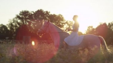 LENS FLARE: Gorgeous young brunette woman horseback riding at golden sunset.