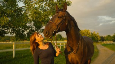Kafkas kızı, kaslı kahverengi aygırına sevgiyle bakıyor..