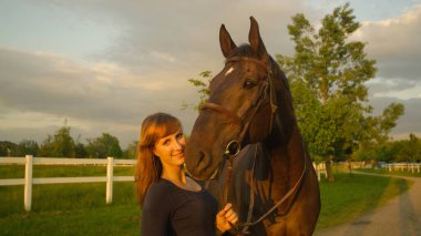 Atın dizginlerini tutarken kameraya bakan sevgi dolu bir kadın..