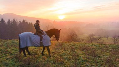 Genç bir kadın kışın kırsalda aygır gibi battaniyeyle dolaşıyor..