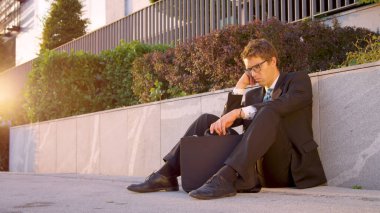 SUN FLARE Young Caucasian man sitting on the street and mourns after being fired
