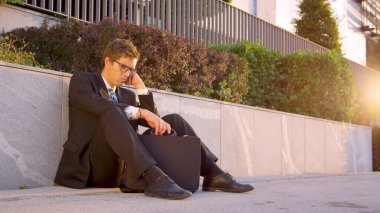 LENS FLARE: Hopeless yuppie sitting on the asphalt pavement after losing his job