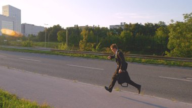 Güneşli bir sabahta takım elbiseli ve kravatlı genç adam ofisine koşuyor..