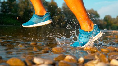 CLOSE UP: Athletic young man running in refreshing glassy stream on a sunny day