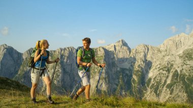 Smiling young Caucasian woman and man hiking in the breathtaking mountains.