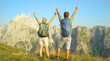 Unrecognizable young tourists celebrate hiking up the mountain in the Alps.