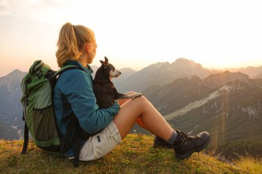 CLOSE UP: Girl sits on mountaintop and pets her dog while observing the nature.