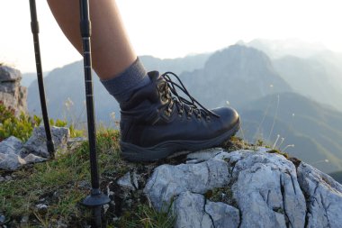 CLOSE UP: Active girl in hiking boots rests at the summit to watch the sunrise.