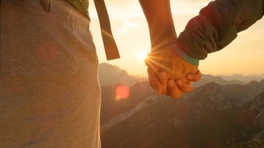 LENS FLARE Man and woman hold hands while observing the sunrise in the mountains clipart