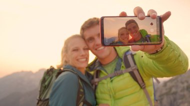 CLOSE UP Smiling man holds up a smartphone while taking a selfie with girlfriend