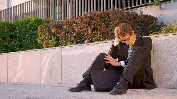 Depressed young Caucasian yuppie sitting on the sidewalk after going bankrupt. — Stock Photo, Image