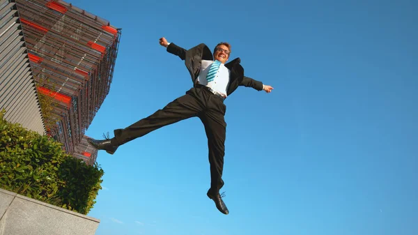 LOW ANGLE Ecstatic Caucasian businessman jumps in the air with arms outstretched — Stock Photo, Image