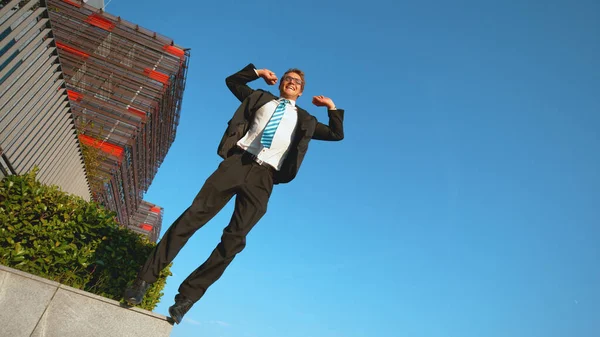 LOW ANGLE: Smiling Caucasian businessman jumps off ledge with arms outstretched. — Stock Photo, Image