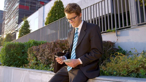 Sluiten: Gelukkige Kaukasische yuppie zittend op een betonnen richel en geld tellend. — Stockfoto