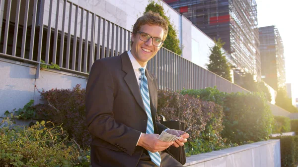 SUN FLARE: Excited businessman looks at the camera while counting his money. — Stock Photo, Image