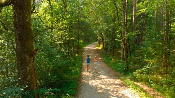 AERIAL: Voando atrás de casal apto irreconhecível correndo pela trilha da floresta. — Fotografia de Stock