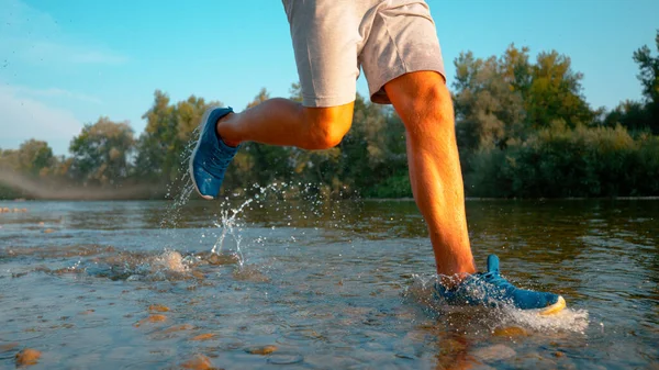 LOW ANGLE: Young sportsman jogs down the shallow river flowing through forest. —  Fotos de Stock