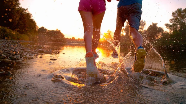 CLOSE UP Golden evening sunbeams shine on active couple jogging in shallow river — Foto de Stock
