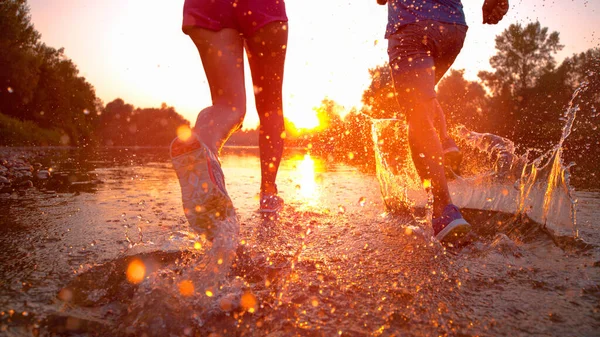 CLOSE UP: Athletic couple jogs in the cold stream water at beautiful sunset. — Stock Photo, Image