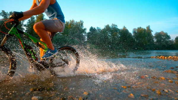 ZAMKNIJ SIĘ: Sportowiec chlapie szklaną wodą podczas jazdy na rowerze wzdłuż strumienia. — Zdjęcie stockowe