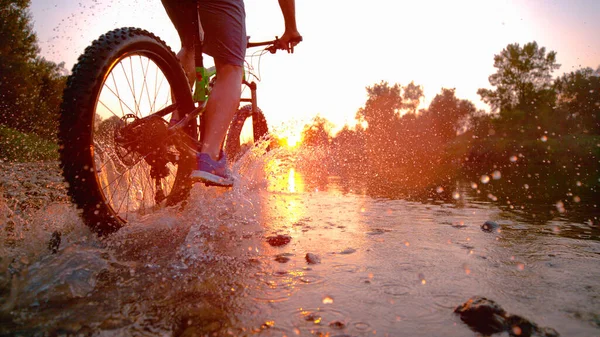 LENS FLARE: Sportsman riding his bicycle in the shallow stream towards sunset. — Stock Photo, Image