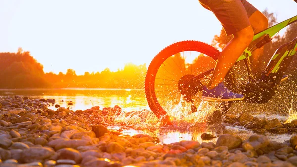 Movimiento lento CERRAR Hombre irreconocible MTB ciclismo en río poco profundo al atardecer —  Fotos de Stock