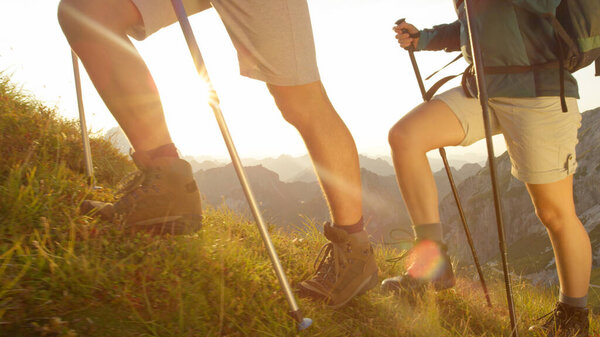 CLOSE UP: Unrecognizable hikers wearing leather boots walking up a grassy hill.