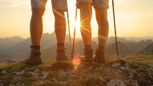 SUN FLARE: Active man and woman in hiking boots walk up to the mountain peak.