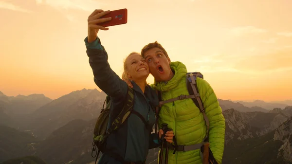 PORTRAIT: Pareja senderista tonta haciendo caras graciosas mientras toma selfies al atardecer . — Foto de Stock