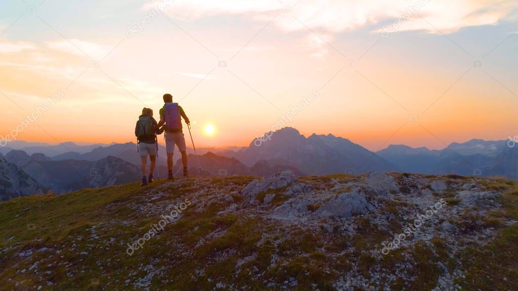 AERIAL: Unrecognizable hiker couple observes evening landscape from mountaintop.