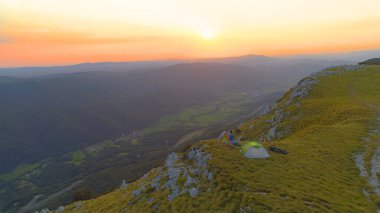 Aktif çift bir dağın kenarında durur ve güneşin batışını seyreder..