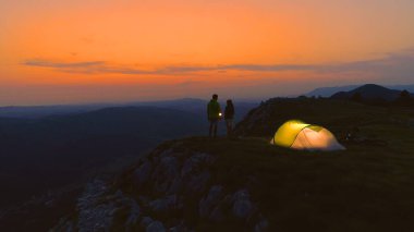 AERIAL: Flying over active young couple observing the sunrise by their tent