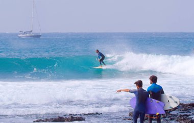 Cool surfer dude carving a beautiful blue barrel wave as friends watch him.
