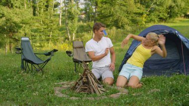 Active tourist couple camping in the wilderness gets swarmed by irritating bugs.