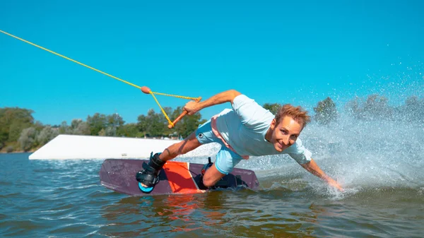 Κοντινό πλάνο: όμορφος άνθρωπος wakeboarding κάνει ένα χέρι σύρετε και πιτσιλάει το νερό. — Φωτογραφία Αρχείου