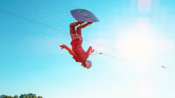 Cinematografische opname van de mens die over de zon draait tijdens het wakeboarden. — Stockfoto