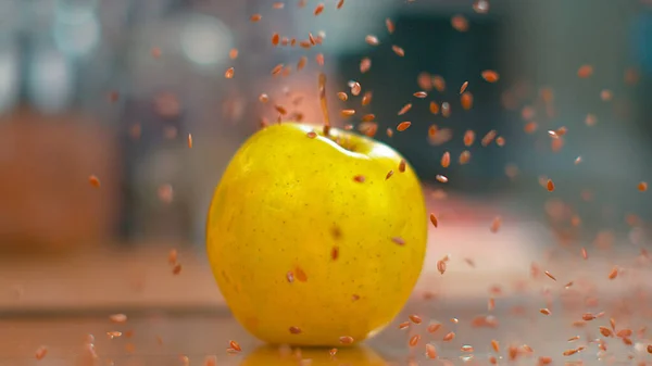 MACRO, DOF: Pequeñas semillas de lino marrón caen del aire y caen sobre la manzana amarilla . —  Fotos de Stock